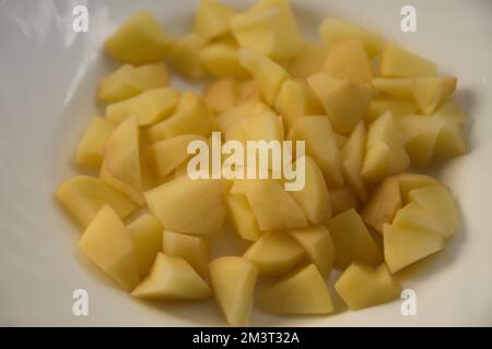 Pommes de terre fraîchement pelées et coupées en dés sur une assiette blanche comme fond prêt à faire des frites Banque D'Images
