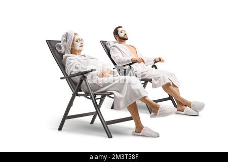 Homme et femme dans des peignoirs blancs avec masques de détente sur des chaises isolées sur fond blanc Banque D'Images