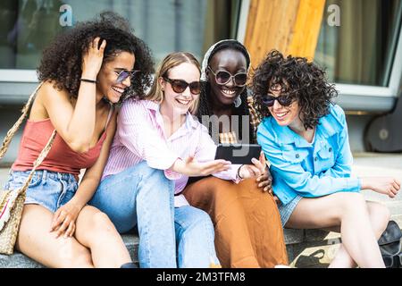 Quatre jolies jeunes femmes regardant l'écran de l'appareil de smartphone et souriant, génération z étudiante s'amusant dans la ville Banque D'Images