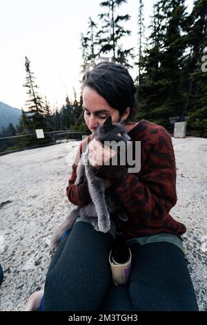 Jeune 30s femme caucasienne tient son chat bleu russe gris et lui donne des amours dans la forêt sauvage pendant qu'elle est dehors avec son mari à une route populaire tr Banque D'Images