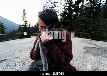 Jeune 30s femme caucasienne tient son chat bleu russe gris et lui donne des amours dans la forêt sauvage pendant qu'elle est dehors avec son mari à une route populaire tr Banque D'Images