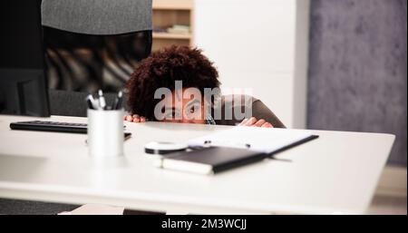 Un homme effrayé se cache derrière le bureau dans la chambre Banque D'Images