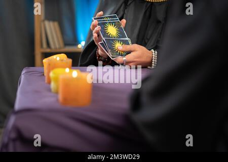 Gros plan d'une fortune tellers main tenant des cartes de tarot sur une table avec des bougies, une session de prévision future pour un client Banque D'Images