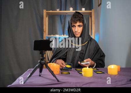 Lecteur de Tarot cueillant des cartes de tarot qui se trouvent face vers le bas sur la table près de bougies allumées. fortune teller en ligne à l'aide d'un smartphone. Bougie dans l'obscurité.Tarot Banque D'Images