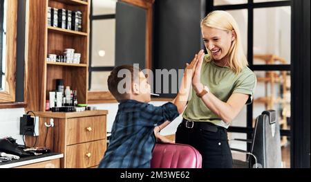 De bons cheveux mettent tout le monde dans une bonne humeur. un adorable petit garçon donnant à son coiffeur un haut cinq à l'intérieur d'un salon. Banque D'Images