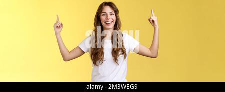 Joyeux amusé heureux animé jeune fille longue coupe de cheveux bouclés lever les mains pointant vers le haut sourire Toothy heureusement caméra présenter une excellente variante suggérer Banque D'Images