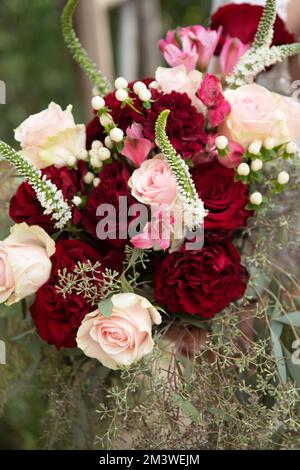 Mariée aux demoiselles d'honneur en robe magenta bordeaux avec fleurs de mariage - roses rouges et blanches profondes avec feuilles d'eucalyptus épépinées Banque D'Images