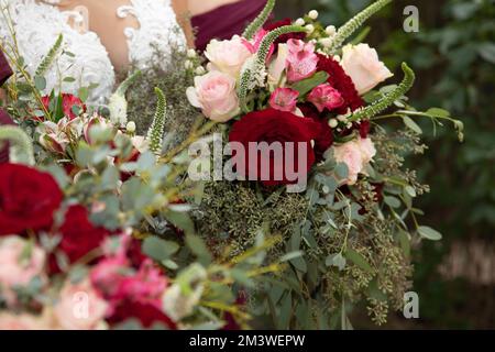 Mariée aux demoiselles d'honneur en robe magenta bordeaux avec fleurs de mariage - roses rouges et blanches profondes avec feuilles d'eucalyptus épépinées Banque D'Images