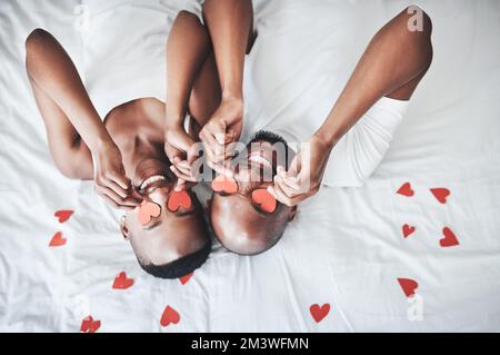 Réveillez-vous le jour de la Saint Valentin. un jeune couple heureux jouant avec des coeurs rouges coupés dans le lit à la maison. Banque D'Images
