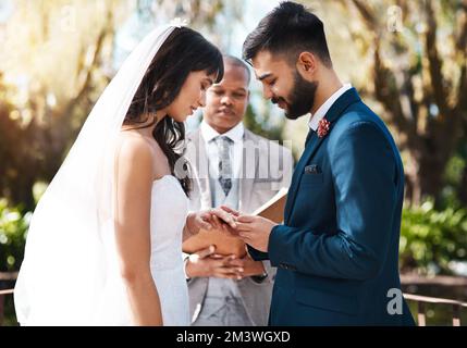 Cet anneau est un symbole de mon amour unying pour vous. un jeune marié affectueux glissant un anneau sur son doigt de mariée tout en se tenant sur l'autel Banque D'Images