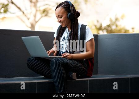 Blogging en plein air est toujours amusant. une jeune femme attirante qui écoute de la musique et utilise son ordinateur portable tout en se relaxant à l'extérieur. Banque D'Images
