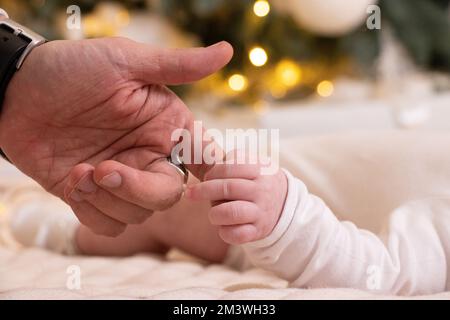 La main du papa tient la main d'un nouveau-né sous l'arbre du nouvel an, l'amour, la main d'un nouveau-né Banque D'Images