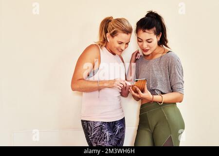 Theres une pose de yoga que nous avons essayé. deux jeunes femmes utilisant un smartphone pendant un cours de yoga. Banque D'Images