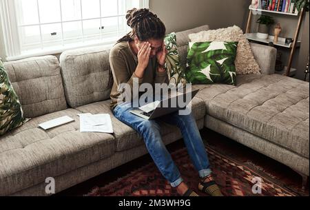 Je dois me concentrer sur ce point. un jeune homme concentré qui travaille sur un ordinateur portable et qui fait de la paperasse tout en étant assis sur un canapé à la maison pendant la journée. Banque D'Images