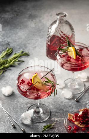 Deux verres de cocktail glacé de Noël à la grenade avec romarin et citron sur fond texturé gris. Boisson de fête de Noël. Orientation verticale Banque D'Images