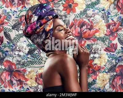 Tombez amoureux de la fabuleuse reine que vous êtes. Photo studio d'une belle jeune femme portant une tête d'enveloppement africaine traditionnelle contre une fleur Banque D'Images