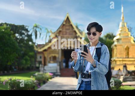 Homme souriant touriste tenant une carte de crédit et utilisant un smartphone pour le paiement en ligne ou de vérifier son compte bancaire Banque D'Images