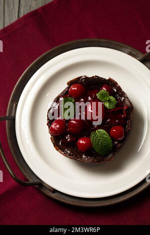 Dessert au chocolat avec cerises et menthe sur une assiette sur fond bordeaux Banque D'Images