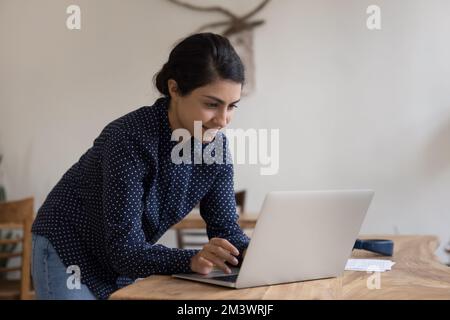 Concentré jeune indienne heureuse utilisatrice d'ordinateur portable femme debout sur le lieu de travail Banque D'Images