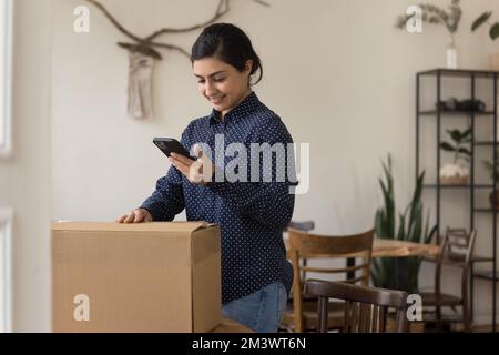 Jeune femme indienne positive emballant une boîte en carton à la maison Banque D'Images