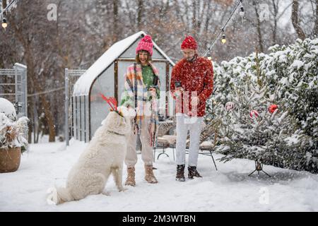 Jeune famille avec un chien dans la cour enneigée pendant les vacances d'hiver Banque D'Images