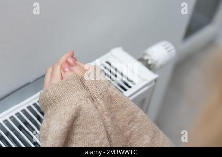 Les mains des femmes essaient de rester au chaud sur un radiateur en aluminium. Une femme se réchauffe près d'un radiateur en hiver pendant la crise énergétique en Europe. Banque D'Images