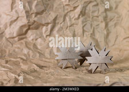 Trois flocons de neige de Noël faits main en carton fabriqués à partir d'un tube de papier toilette isolé sur une surface et un fond de papier froissé. Banque D'Images