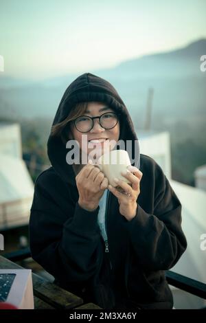femme d'âge moyen, souriante et souriante, avec un visage de bonheur tenant une tasse de café à la main assise à l'extérieur Banque D'Images