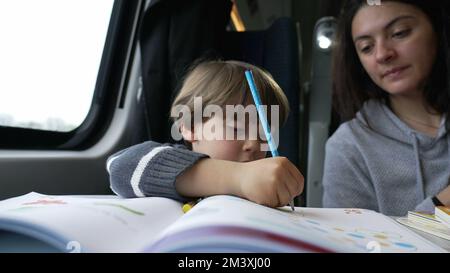 Un petit enfant fait ses devoirs tout en voyageant en train avec l'aide et le soutien de sa mère. Dessin de garçon avec stylo à colorier crayon stylo sur papier sur le transport Banque D'Images