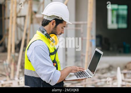 le contremaître de l'ingénieur en construction travaille en contact avec un ordinateur portable sur le chantier de construction Banque D'Images