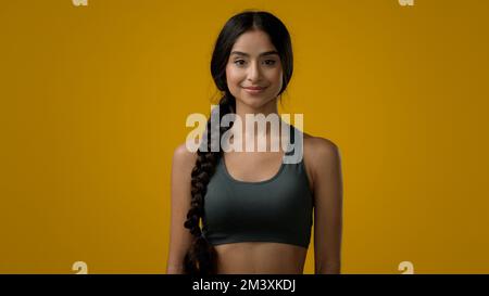 Ethnique 20s femme indienne sport dame souriant multiracial forte fille mince entraîneur sportif coureur de yoga posant dans jaune studio athlète femelle regardant Banque D'Images