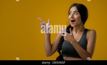 Portrait ethnique indienne sport femme fille femme femme dans le studio jaune arrière-plan pointant les doigts montrant sur vide espace de copie pour le spectacle publicitaire Banque D'Images