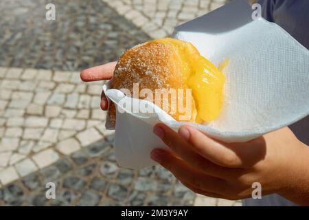 Main tenant Bola de Berlim ou Berlim ball, une pâtisserie portugaise faite à partir d'un beignet frit rempli de crème d'éggy douce et roulé dans du sucre croquant. Banque D'Images