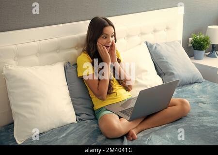 Adolescente étudie à la maison sur lit avec ordinateur portable. Expressif émotionnel excitée jeune fille. Banque D'Images