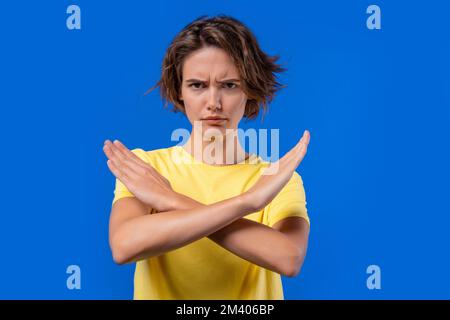 Une femme désintéressée qui n'approuve pas le geste de signe DE main de croisement. Refuser, rejeter, pas d'accord. Portrait de la jeune femme sur fond bleu, temporisation Banque D'Images