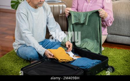 Asiatique romantique retraite couple emballer vêtements sac de voyage valise ensemble sur le sol à la maison Banque D'Images