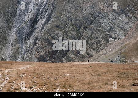 Une vue sur les personnes marchant devant un grand mur d'une haute montagne dans un paysage dans les Pyrénées près du pic Bastitents Banque D'Images