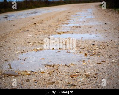 des nids-de-poule remplis d'eau sur une route sablonneuse après la pluie Banque D'Images