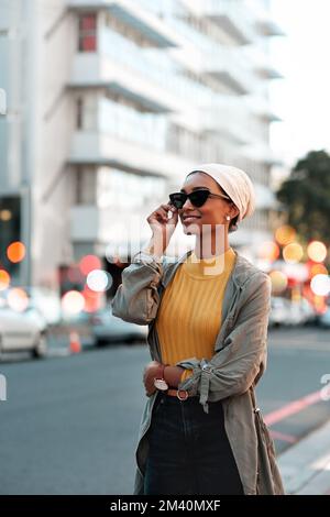 J'ai apprécié mon séjour en ville. une jeune femme attrayante portant des lunettes de soleil et un hijab tout en se tenant seule dans la ville. Banque D'Images