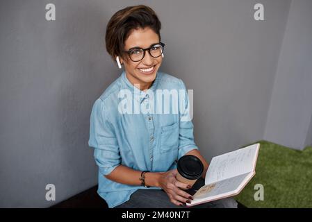 Je m'en charge. une jeune femme d'affaires attirante assise seule sur un banc et lisant un ordinateur portable tout en buvant du café. Banque D'Images