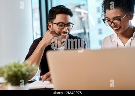 C'est très beau. deux jeunes collègues d'affaires assis ensemble et regardant un ordinateur portable au bureau. Banque D'Images