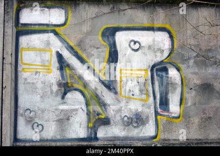 Graffiti d'un grand mot composé de grandes lettres Elio N dessinées dans un lapdog de couleur blanc, noir, jaune sur une clôture de ciment brun-gris. Banque D'Images