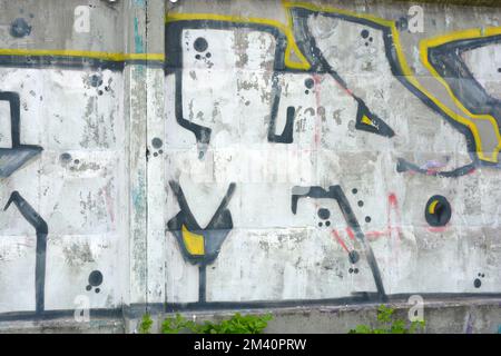 Graffiti d'un grand mot composé de grandes lettres Elio N dessinées dans un lapdog de couleur blanc, noir, jaune sur une clôture de ciment brun-gris. Banque D'Images