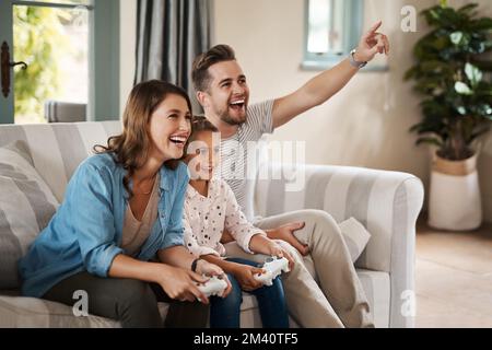 Au coeur de chaque maison se trouve la convivialité. une jeune famille heureuse jouant à des jeux vidéo sur le canapé à la maison. Banque D'Images