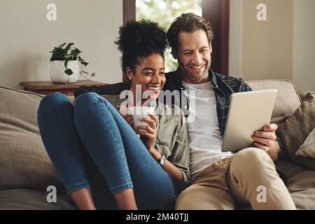 Ces applications nous permettent de toujours nous divertir. un jeune couple heureux utilisant une tablette numérique ensemble tout en se relaxant sur un canapé à la maison. Banque D'Images