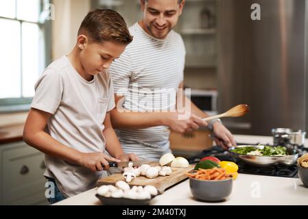 Petit chef en préparation. un jeune garçon aidant son père à cuisiner dans la cuisine. Banque D'Images