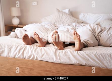 Les dimanches sont des jours de sommeil. un couple pieds poking dehors de sous les draps de lit. Banque D'Images