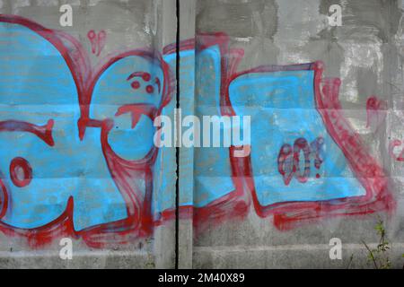 A lettres bleues et grises et épaisses lignes rouges et cerises avec bordures rouges. Un graffiti représentant le mot KOWAH est sur une clôture en béton grise et brune. Banque D'Images