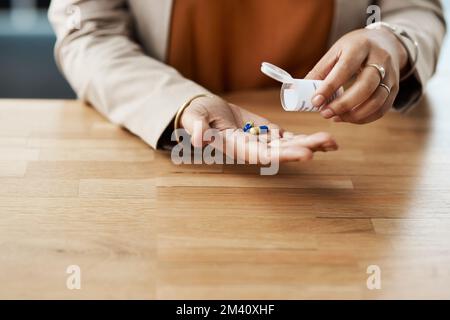 Combien dois-je prendre ? une femme d'affaires méconnaissable prenant des pilules d'une boîte à pilules pendant qu'elle se trouve dans son bureau. Banque D'Images