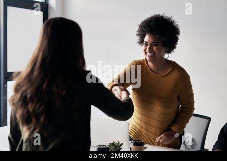Nous sommes impatients de commencer à travailler avec vous. deux jeunes femmes d'affaires se saluent l'une l'autre par une poignée de main avant de s'asseoir au bureau. Banque D'Images